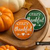 SnapAccents snap jewelry buttons with "crazy thankful" text in white on orange and green backgrounds, featuring heart and arrow design, displayed on wooden tray with small pumpkins, perfect for fall and Thanksgiving accessories.