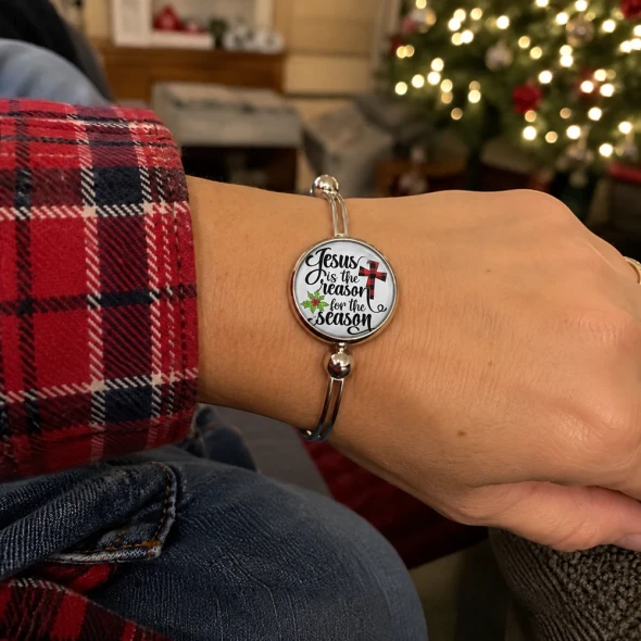 Round SnapAccents snap jewelry charm with "Jesus is the reason for the season" text, featuring a red and black buffalo plaid cross and green holly leaves, set against a festive red background with snowflake patterns.