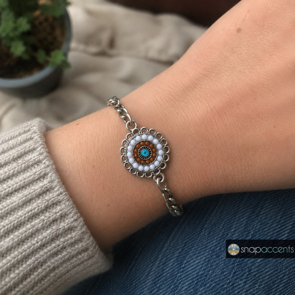 snap jewelry bracelet with a round charm featuring concentric circles of white and brown beads and a central aqua rhinestone with a scalloped silver edge