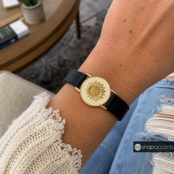 snap jewelry bracelet with a black leather band featuring a round cream snap charm stamped with a gold sunflower design