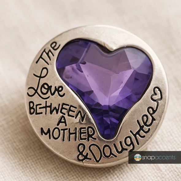 Round silver SnapAccents snap jewelry charm with a faceted purple heart-shaped gemstone in the center and engraved text reading "The Love Between A Mother & Daughter" on the outer edge.