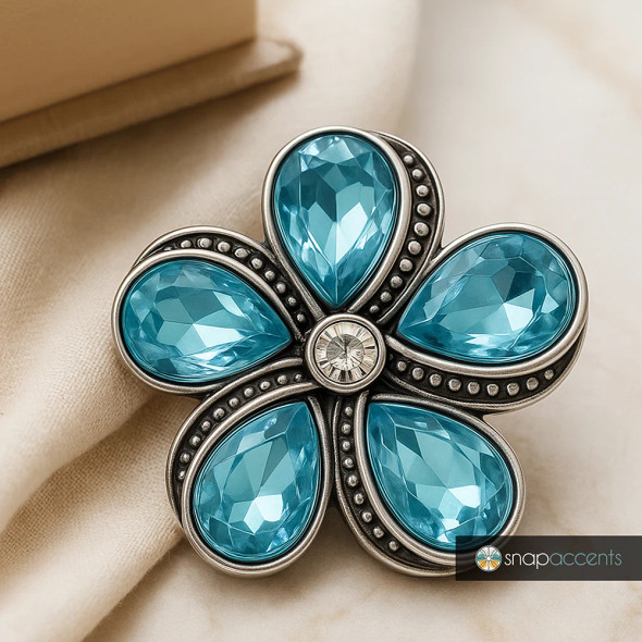 SnapAccents snap jewelry flower charm with five large faceted teardrop blue gemstones and a central clear rhinestone, set in antique silver-tone metal with decorative beaded detailing, perfect for interchangeable snap bracelets, necklaces, and accessories.