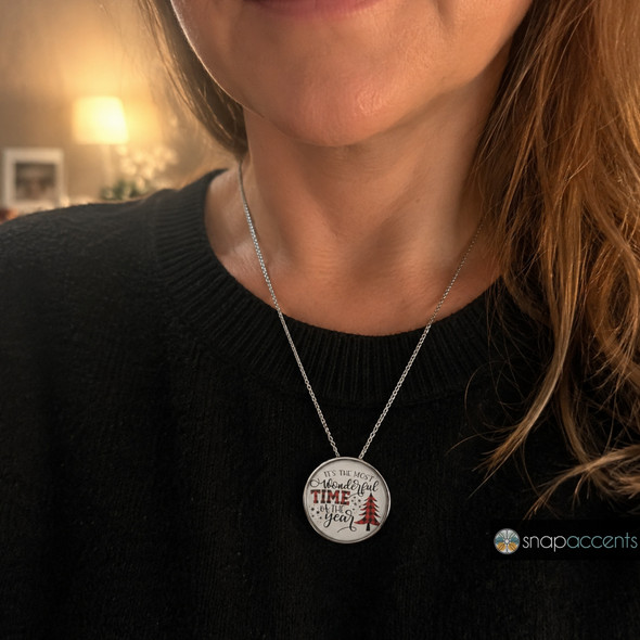 silver necklace with a round snap jewelry charm featuring the phrase It's The Most Wonderful Time Of The Year and a red and black plaid Christmas tree