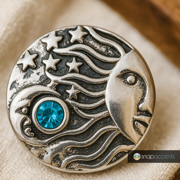 Antique silver-tone SnapAccents snap jewelry button featuring sun and moon design with flowing rays, stars, and a central blue rhinestone accent, perfect for interchangeable charm bracelets and necklaces.
