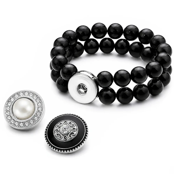 Black beaded double-strand snap bracelet with interchangeable decorative snap charms featuring a pearl surrounded by crystals and a black charm with intricate silver design and central crystal, displayed on a black background with white ribbon, SnapAccents logo visible.