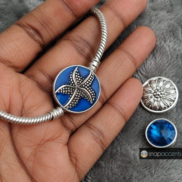 silver-tone starfish snap jewelry charm with textured dots on a deep blue enamel background installed on a silver snake chain bracelet, shown with two additional snap charms