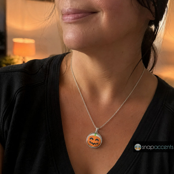 silver necklace with a round snap jewelry charm featuring an orange jack-o-lantern pumpkin with a smiling face and green stem