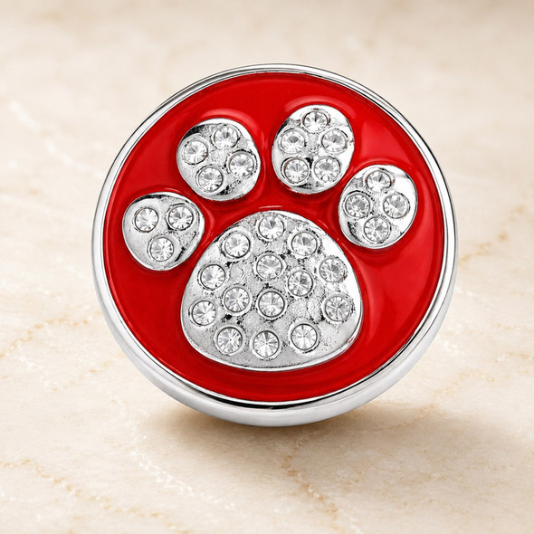 round snap jewelry charm with a red enamel background and a silver dog paw design encrusted with clear rhinestones