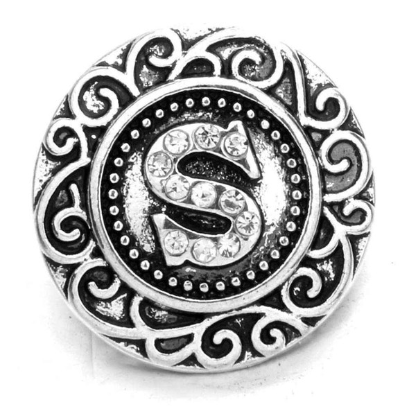 round silver snap jewelry charm with filigree design and rhinestone-studded letter S in the center