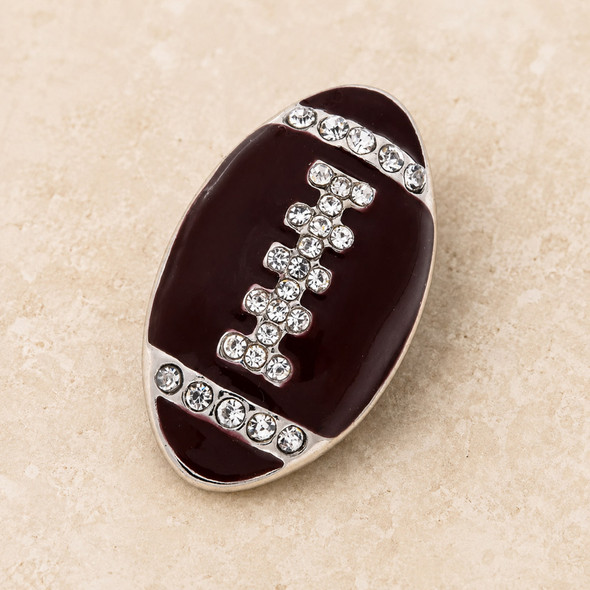 brown enamel football-shaped snap jewelry charm with clear rhinestone laces and accents on a beige surface