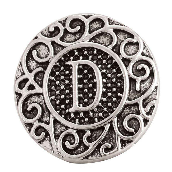round silver snap jewelry charm with intricate filigree design and raised letter D on textured black background