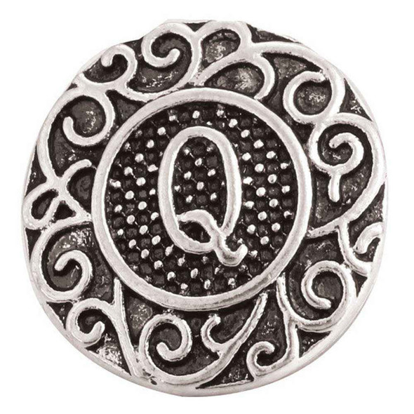 round silver snap jewelry charm with raised letter Q in the center and intricate filigree swirl design on a textured dark background