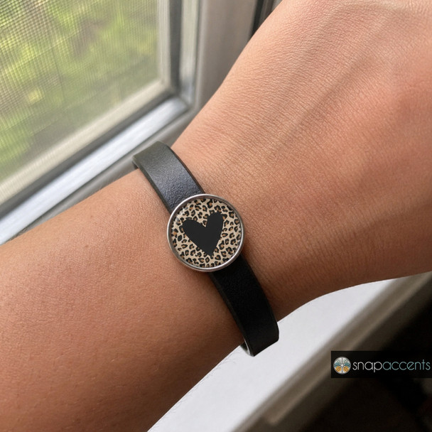snap jewelry bracelet with a round charm featuring a black heart on a brown and black animal print background on a black leather band