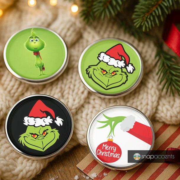 SnapAccents snap jewelry set featuring four Christmas-themed interchangeable snaps with Grinch designs, including Grinch face with Santa hat, Grinch character, and a "Merry Christmas" ornament, displayed on a cozy knitted background with festive greenery and gift wrapping accents.