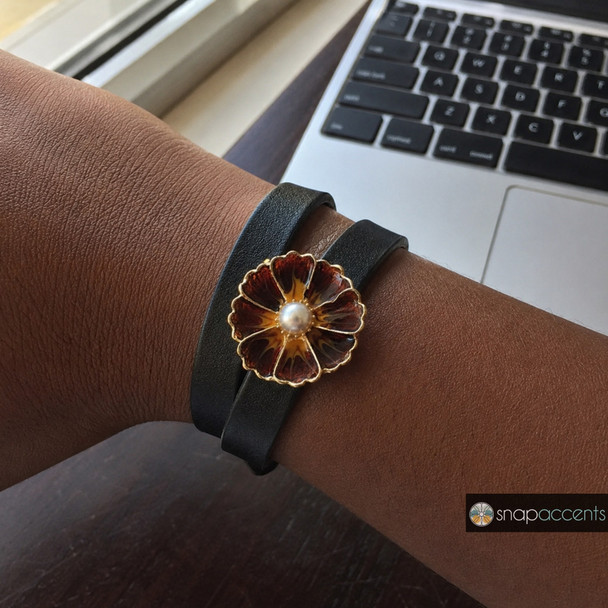 brown enamel flower snap jewelry charm with a white pearl center on a black double-wrap leather bracelet