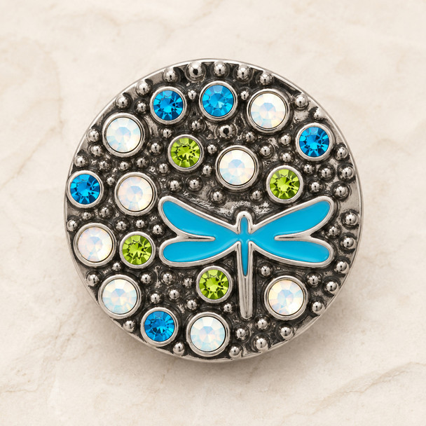 round snap jewelry charm with a blue enamel dragonfly center surrounded by blue, green, and clear rhinestones on a textured gray background
