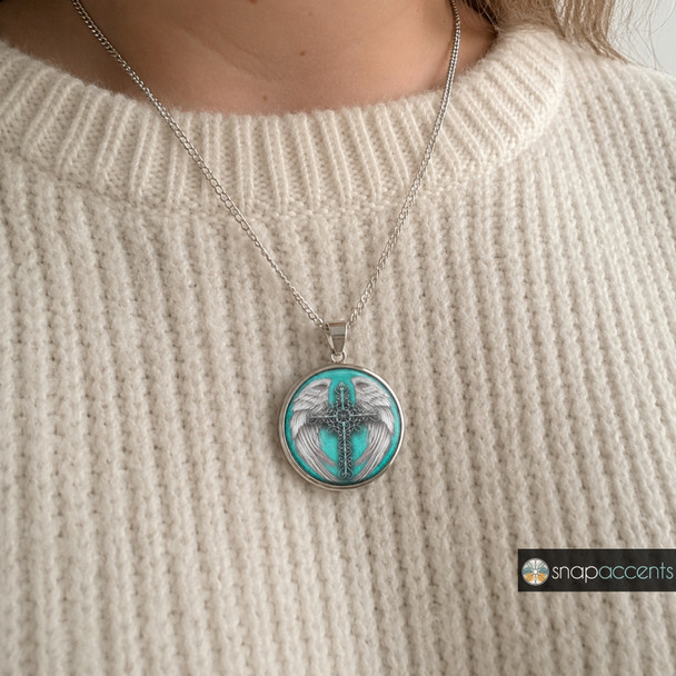 silver necklace with a round turquoise snap jewelry pendant featuring a detailed silver cross with wings design