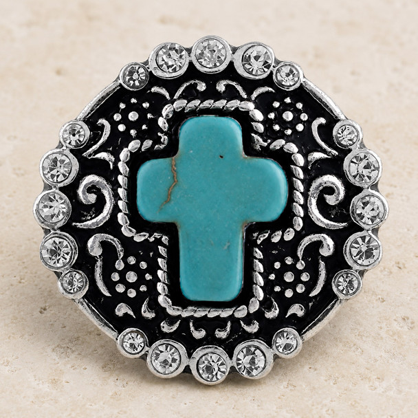 round snap jewelry charm with a turquoise cross center, surrounded by clear rhinestones and silver-toned filigree on a black background