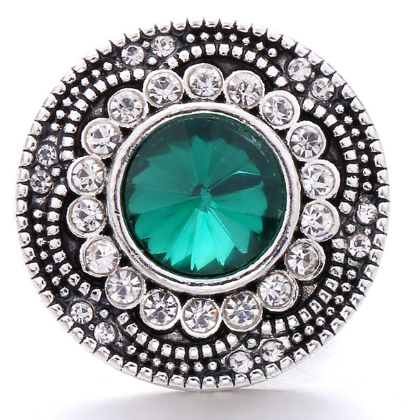 round snap jewelry charm with a faceted green center stone surrounded by two rows of clear rhinestones in a silver-toned setting