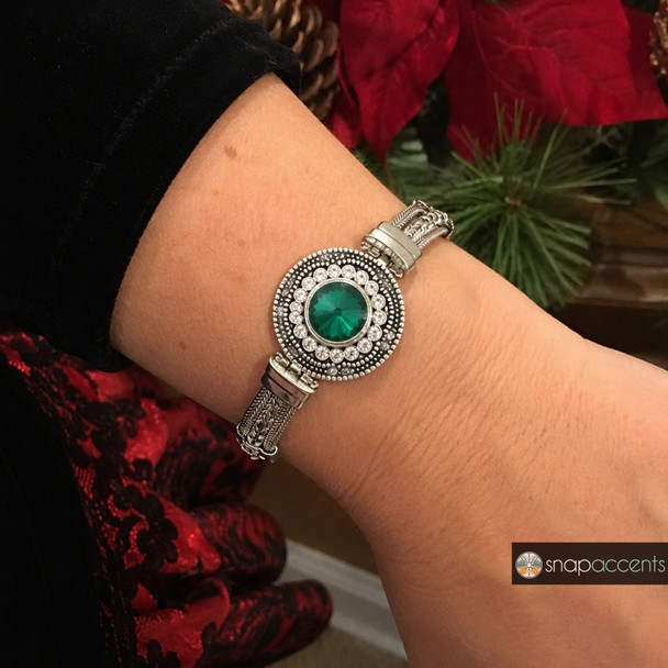 silver-toned snap jewelry bracelet with a round green faceted center stone surrounded by clear rhinestones worn on wrist
