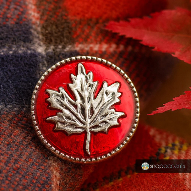 Red SnapAccents snap jewelry button featuring a detailed silver maple leaf design, perfect for fall and Canadian-themed accessories, displayed on a cozy plaid fabric background.
