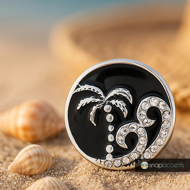 Round SnapAccents snap jewelry charm with silver palm tree and rhinestone wave design on black background, beach-themed accessory on sand with seashells, trendy interchangeable snap button for bracelets and necklaces.
