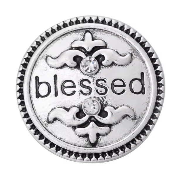 Round silver SnapAccents snap jewelry charm with decorative fleur-de-lis designs, two clear rhinestones, and the word "blessed" engraved in black lettering, perfect for customizable bracelets and necklaces.