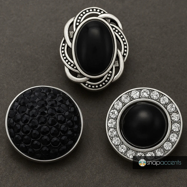 Three SnapAccents snap jewelry pieces featuring black stones and silver-tone settings; one oval with intricate silver detailing, one round with black faceted stones, and one round with black center stone surrounded by clear rhinestones on a dark background.