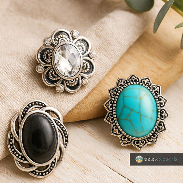 SnapAccents snap jewelry buttons featuring three decorative snap charms with intricate silver-tone metal designs and large oval stones in clear, black, and turquoise colors, perfect for customizable bracelets, necklaces, and accessories. Displayed on a wooden surface with natural fabric background, ideal for boho and vintage style jewelry lovers.