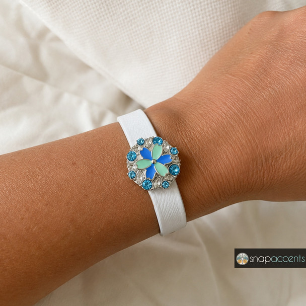snap jewelry bracelet with a white leather band featuring a round floral snap charm with teal and blue petals surrounded by blue and clear rhinestones