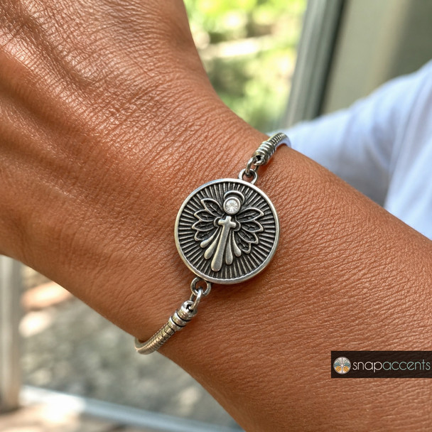 silver snap jewelry bracelet with a round charm featuring a cross over angel wings and a single rhinestone accent