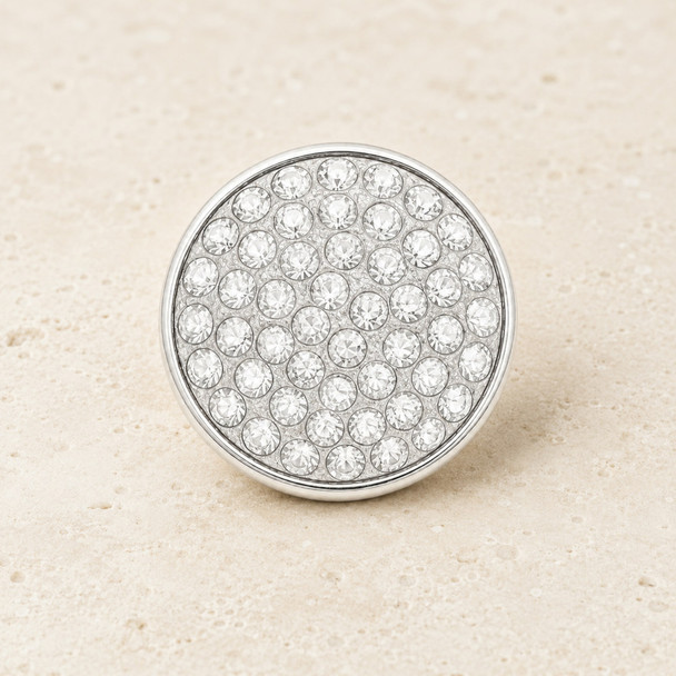 round snap jewelry charm covered with multiple clear rhinestones in a silver-tone setting on a beige textured surface