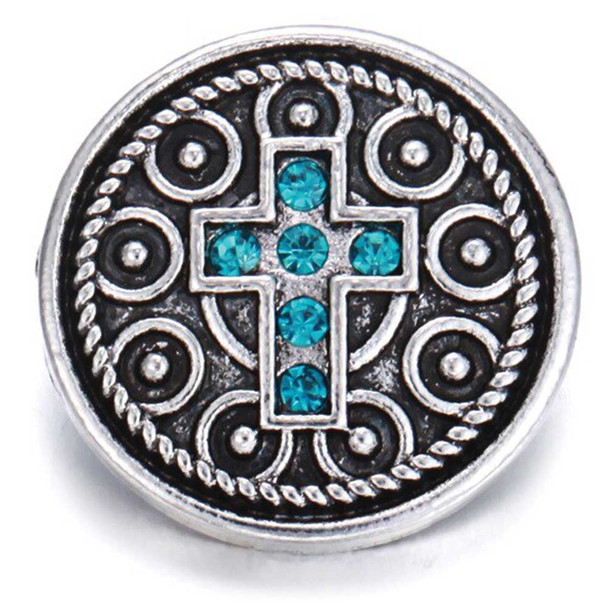 Round silver snap jewelry charm with intricate circular patterns and a central cross adorned with six bright turquoise blue rhinestones, designed for interchangeable SnapAccents accessories.