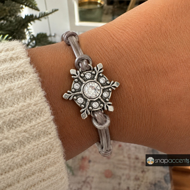silver snowflake snap jewelry charm with clear rhinestones on a gray leather bracelet worn on wrist