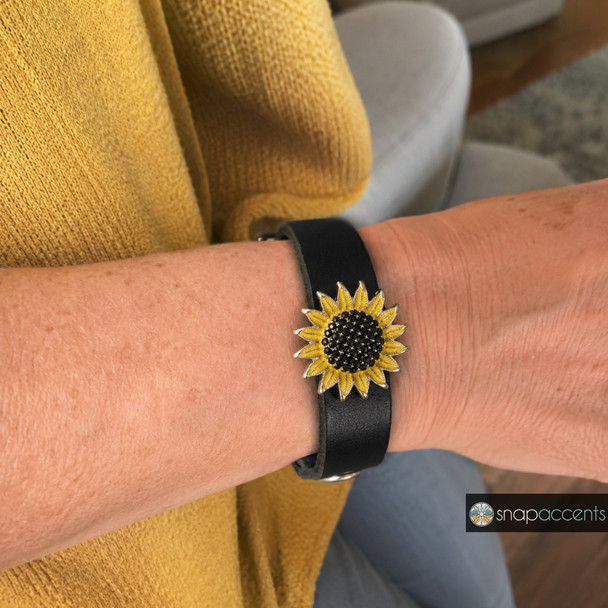 black leather snap jewelry bracelet with a sunflower snap charm featuring yellow enamel petals and a black rhinestone center worn on wrist