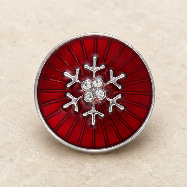 Round red snap jewelry charm with a silver snowflake design accented by four clear rhinestones on a radial enamel background