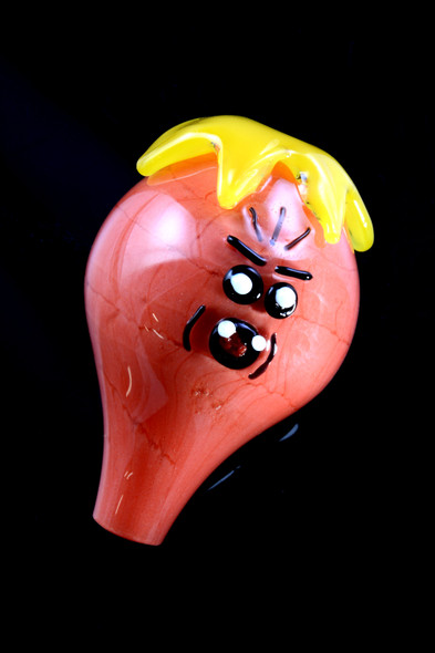 Macro of red glass bubble cap showing cartoon face and yellow drip crown, wholesale head-shop cap, angled close-up on black background.