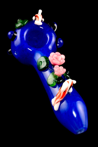 Deep-blue glass koi pond spoon with pink blossoms and green lily pads, angled studio shot on black—wholesale head-shop pipe, compact 4.5" size.