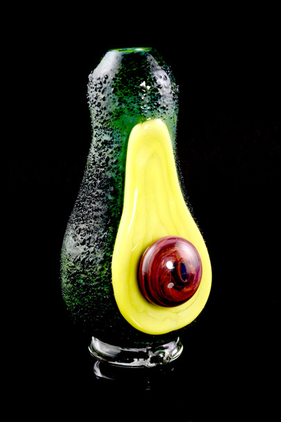 Standalone avocado glass topper, front view on black with textured green peel and yellow flesh—premium retail smoke-shop attachment.