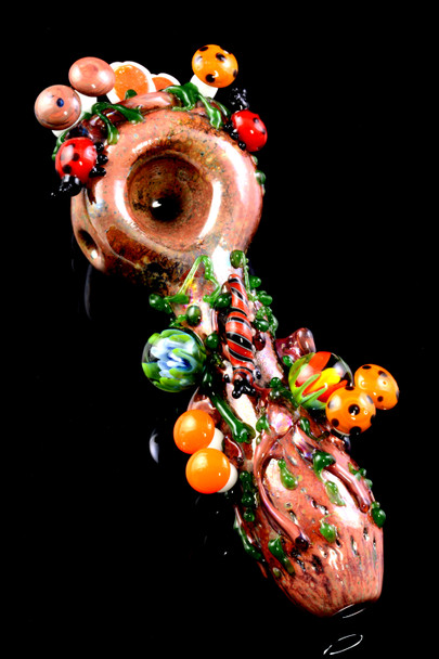 Top-down wholesale photo of 4.5" log-brown glass spoon with ladybugs, orange mushrooms, and vine accents; borosilicate build for head-shop displays.