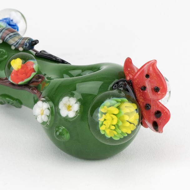 Macro close-up for head-shop supplies highlighting red ladybug, yellow flower marble, and white floral dots on deep green spoon body.