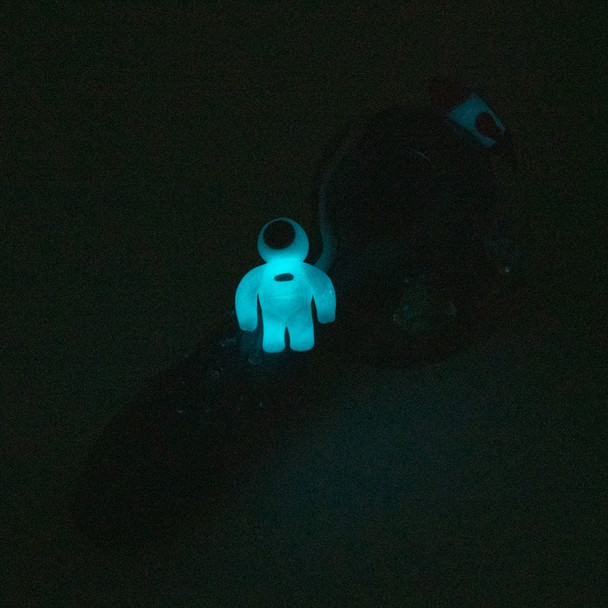 Dark-room photo highlighting glowing teal astronaut on galactic spoon; UV-reactive effect showcased for B2B head-shop buyers.