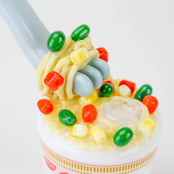 Macro angle on fork and noodle cluster with colorful “veggies,” cup rim and joint seat visible; wholesale product detail for smoke-shop buyers.