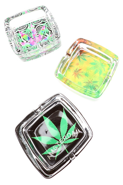 Three square clear glass ashtrays with assorted cannabis leaf patterns in green, yellow, black, and pink