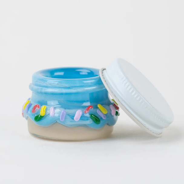Wholesale donut terp jar, 1.5-inch blue glaze with pastel sprinkle glass, white metal lid tilted beside jar, side angle hero shot on clean backdrop.