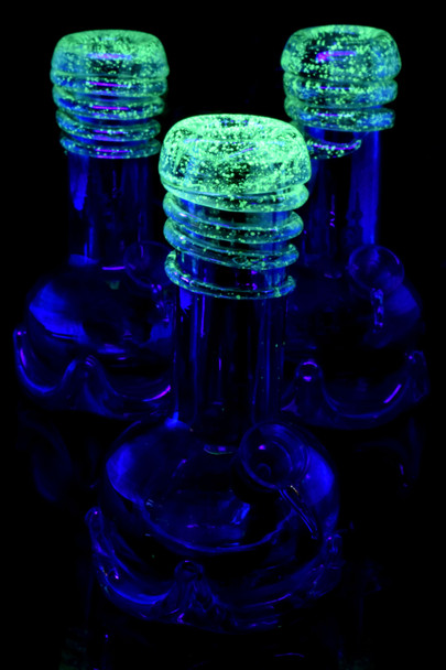 Wholesale 7-in metallic soft glass water pipes glowing green swirl under black-light, triple close-up.