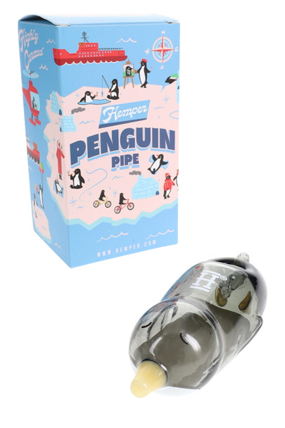 Smoky gray Hemper Penguin 4" glass hand pipe resting before bright blue cartoon Penguin Pipe box, retail-ready setup for head shop shelves.