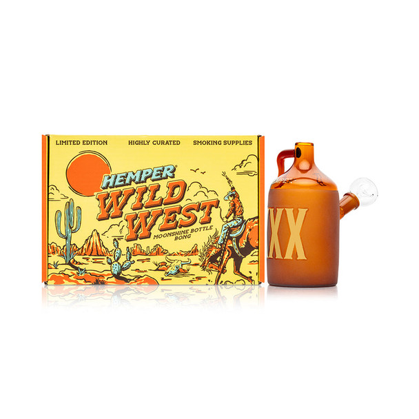 Wide shot of amber moonshine jug bong beside illustrated Hemper Wild West box, hero image for online retail smoke-gear catalogs.