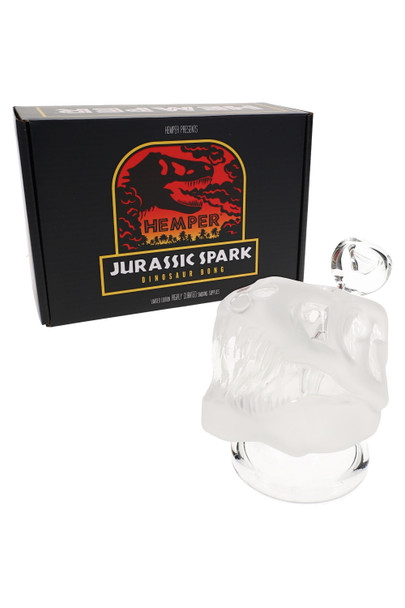 Frosted dinosaur skull Hemper Jurassic Spark bong in front of black red-logo gift box, three-quarter view for head-shop retail display planning.