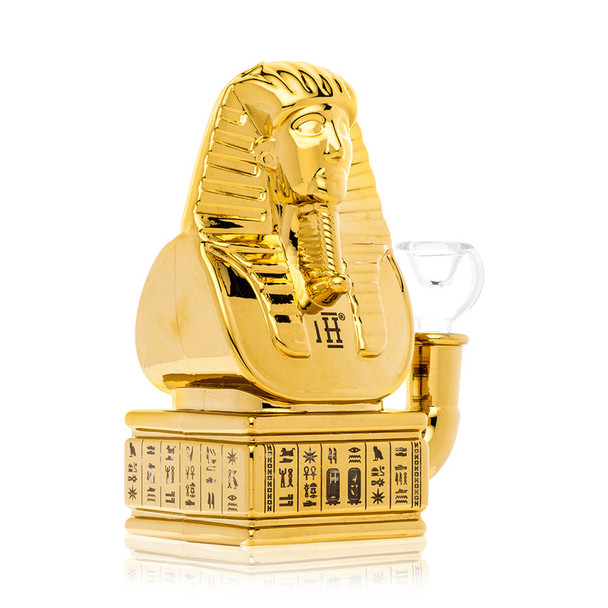 Angled side view of gold pharaoh bust Hemper Ancient Egypt bong showing inline perc base and clear slide bowl, detailed product photo for smoke-shop suppliers.